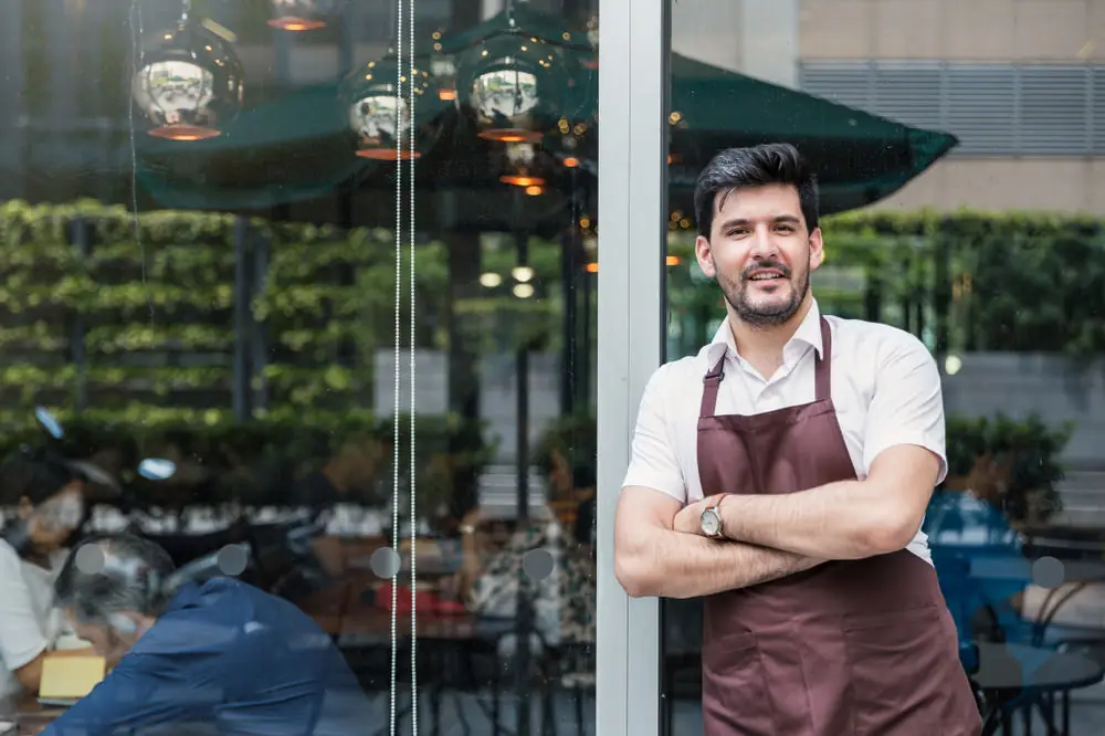 A cafe owner outside his own door, arms folded, in no hurry to sign.