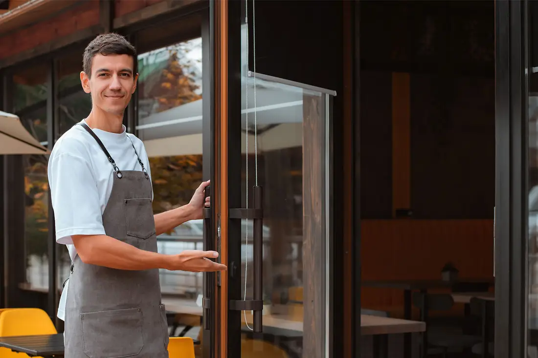A cafe owner holding the door open on the day's trade.